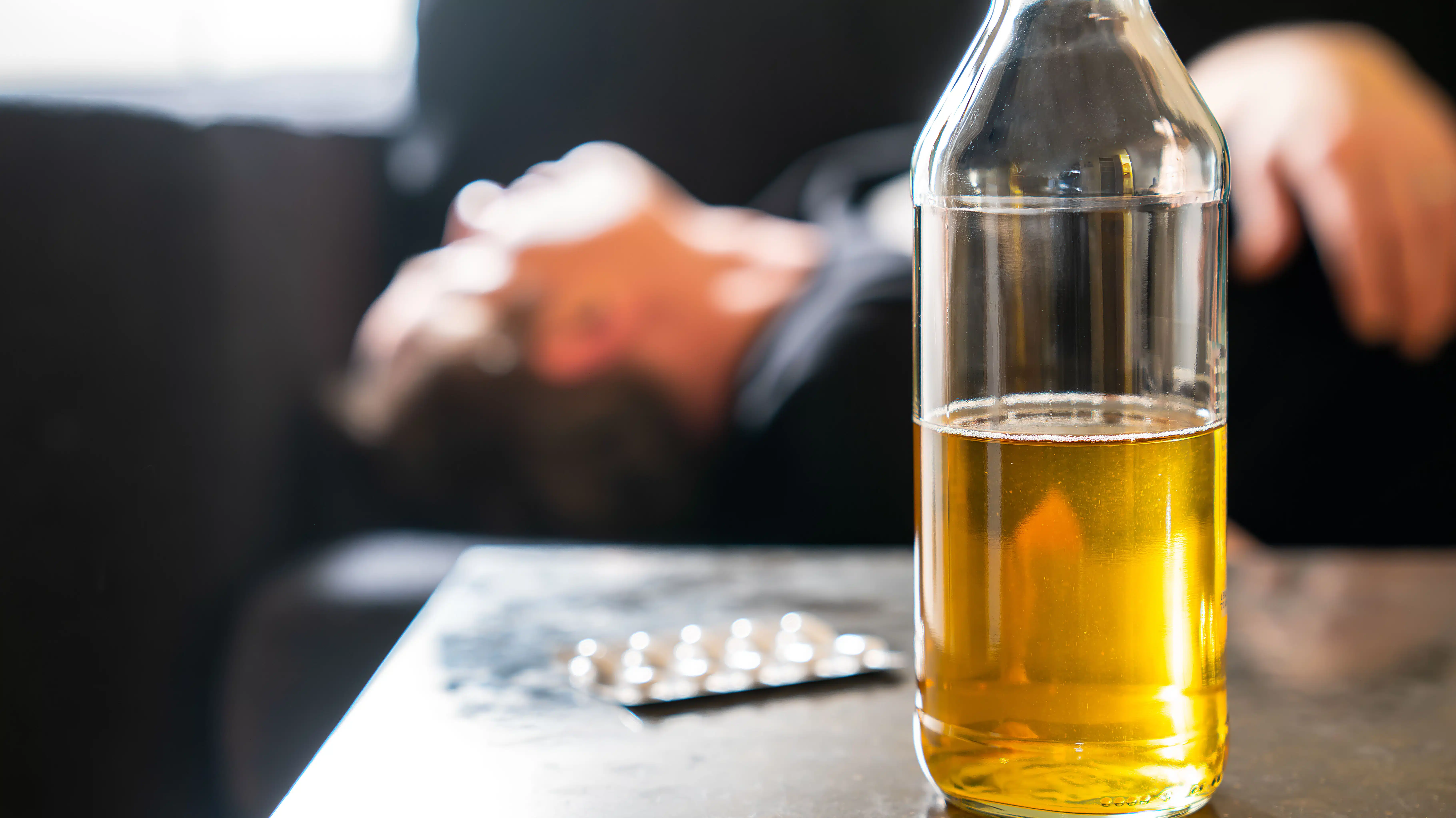 A beer bottle sits on a table next to a blister pack of pills - Can You Drink Alcohol On Painkillers