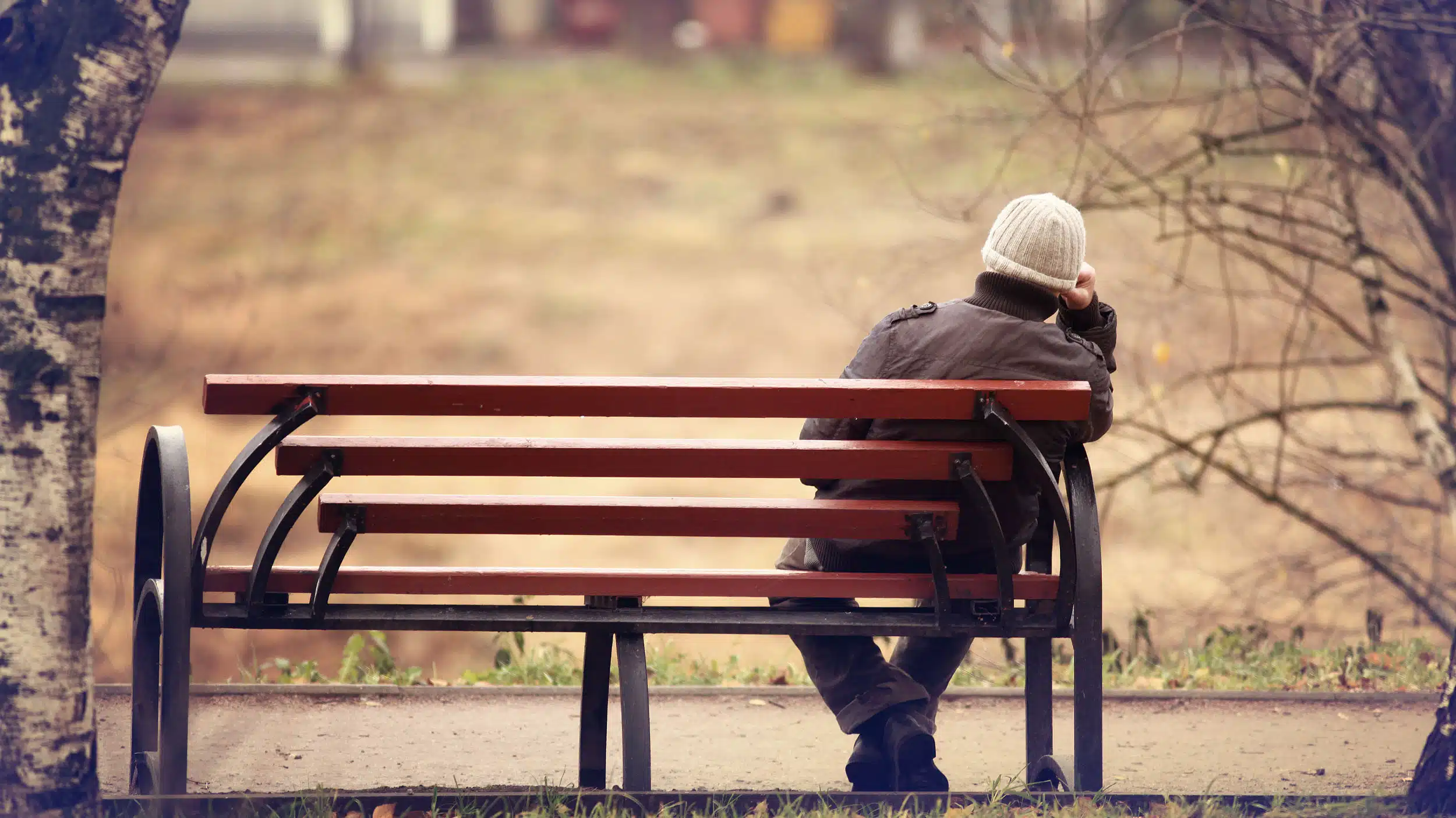 A lonely man sits on a park bench - How Loneliness Contributes To Addiction
