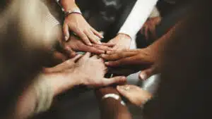 People of multiple races and genders all put their hands in the center of a circle - Mental Health Disorder Patterns In Diverse Populations
