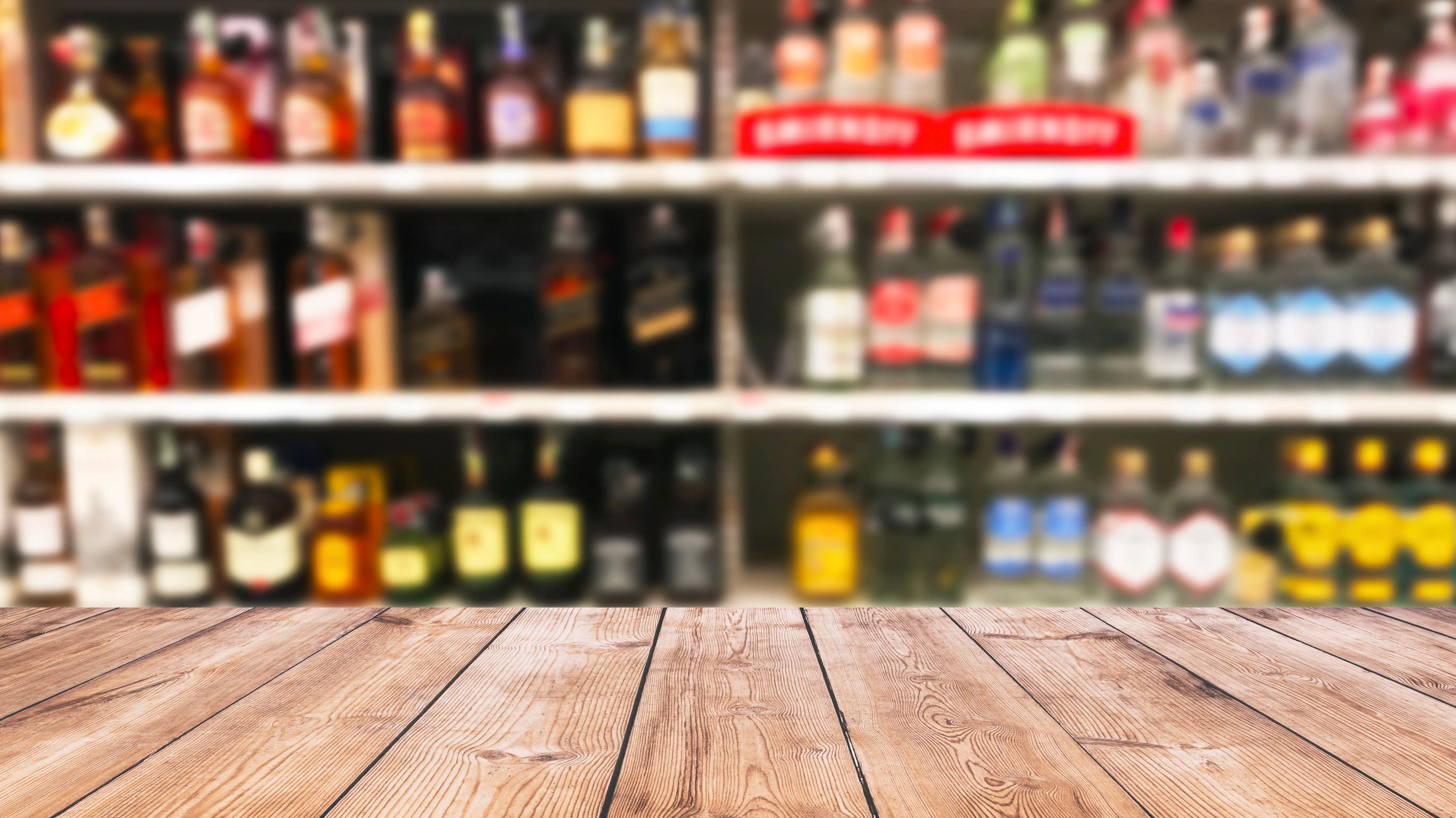 A blurred image of liquor store shelves behind a wooden counter top - Myths About Alcohol Tolerance & Heavy Drinking