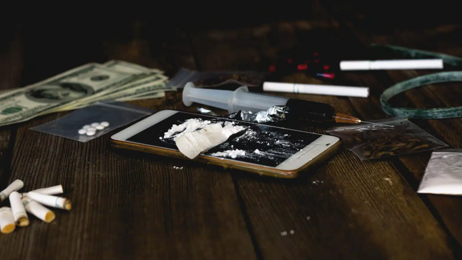 A collection of drug paraphernalia, cash, and a cell phone - Signs Someone May Be Using Drugs