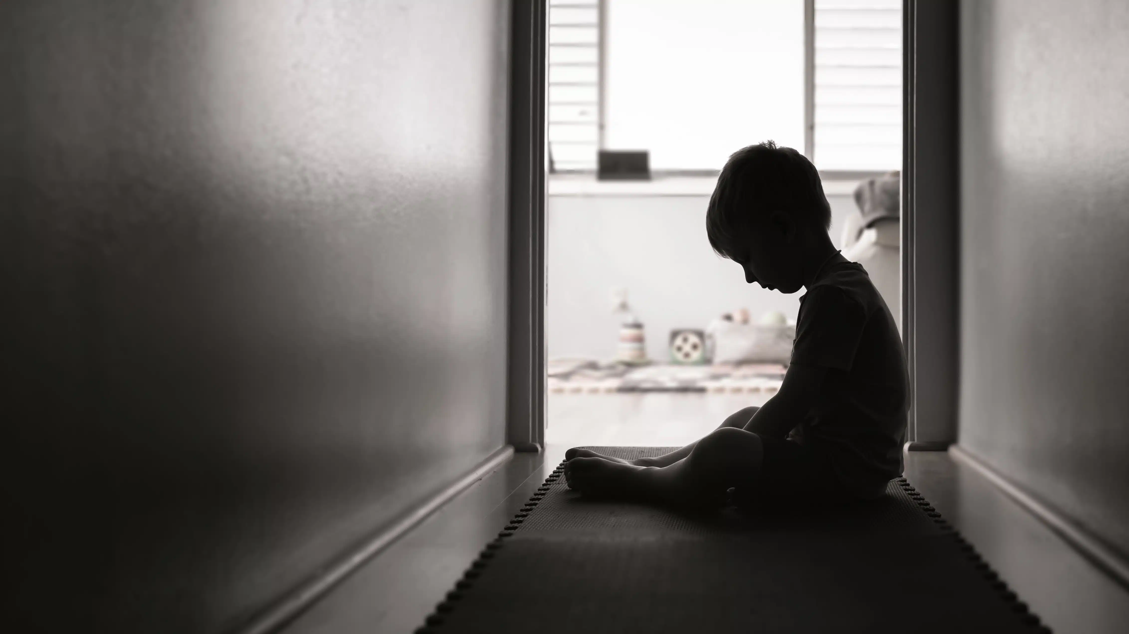 A silhouette of a child sitting alone in a dark hallway - Substance Abuse In The Foster Care System