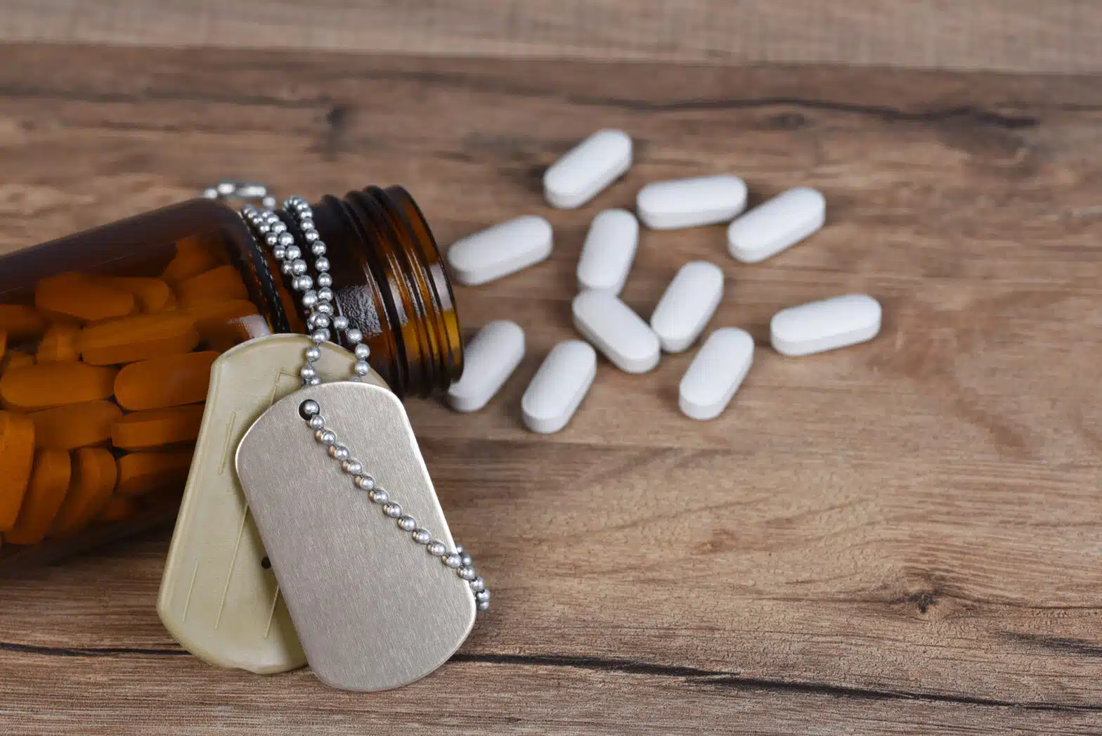 A set of unengraved dog tags is draped over a pill bottle. Pills have fallen out of the bottle - Substance Use Disorders In The United States Military