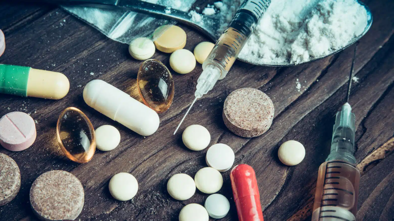 Pills, tablets, syringes, and powder on a wooden table - Top 5 Most Addictive Substances In Massachusetts