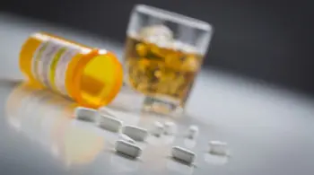 several prescription drugs spilled from a fallen bottle near glass of alcohol.